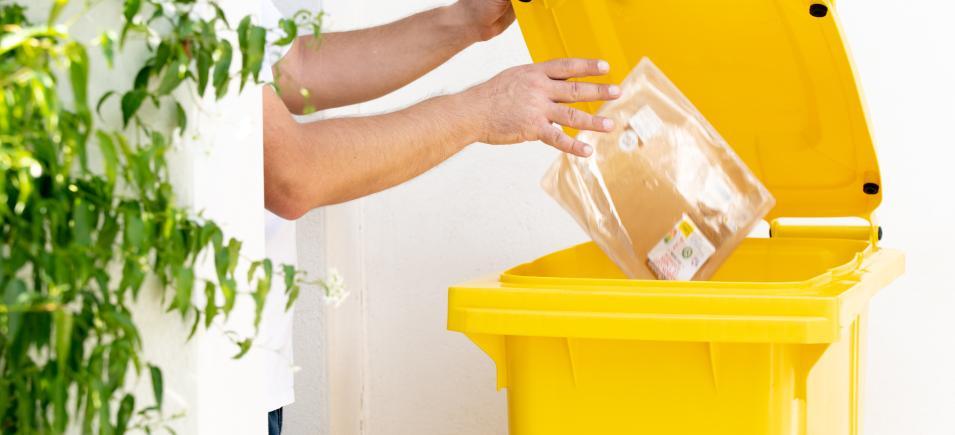 Ceci est une photo où l'on voit une personne jeter un emballage dans son bac jaune individuel de tri 